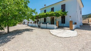 A white building with a gravel driveway, a pergola with vines, and a stone wall.