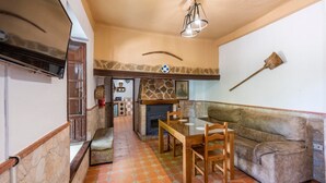 A cozy living area with a stone fireplace, a wooden dining table with chairs, and a cushioned sofa.