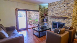 A living room with a stone wall, a glass coffee table, leather sofas, a TV, and a fireplace. - Los Albardinales - Casa Picual Tabernas by Ruralidays (Almería)