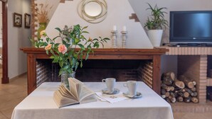 Una sala de estar acogedora con chimenea, una mesa con un libro y dos tazas, y un televisor sobre un mueble.