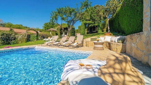 Piscina con sillas de descanso y una mesa con una toalla y gafas de sol.