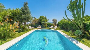 A rectangular swimming pool with clear blue water, surrounded by lush greenery and a few lounge chairs. - Villa Riillo Casarabonela by Ruralidays (Málaga)