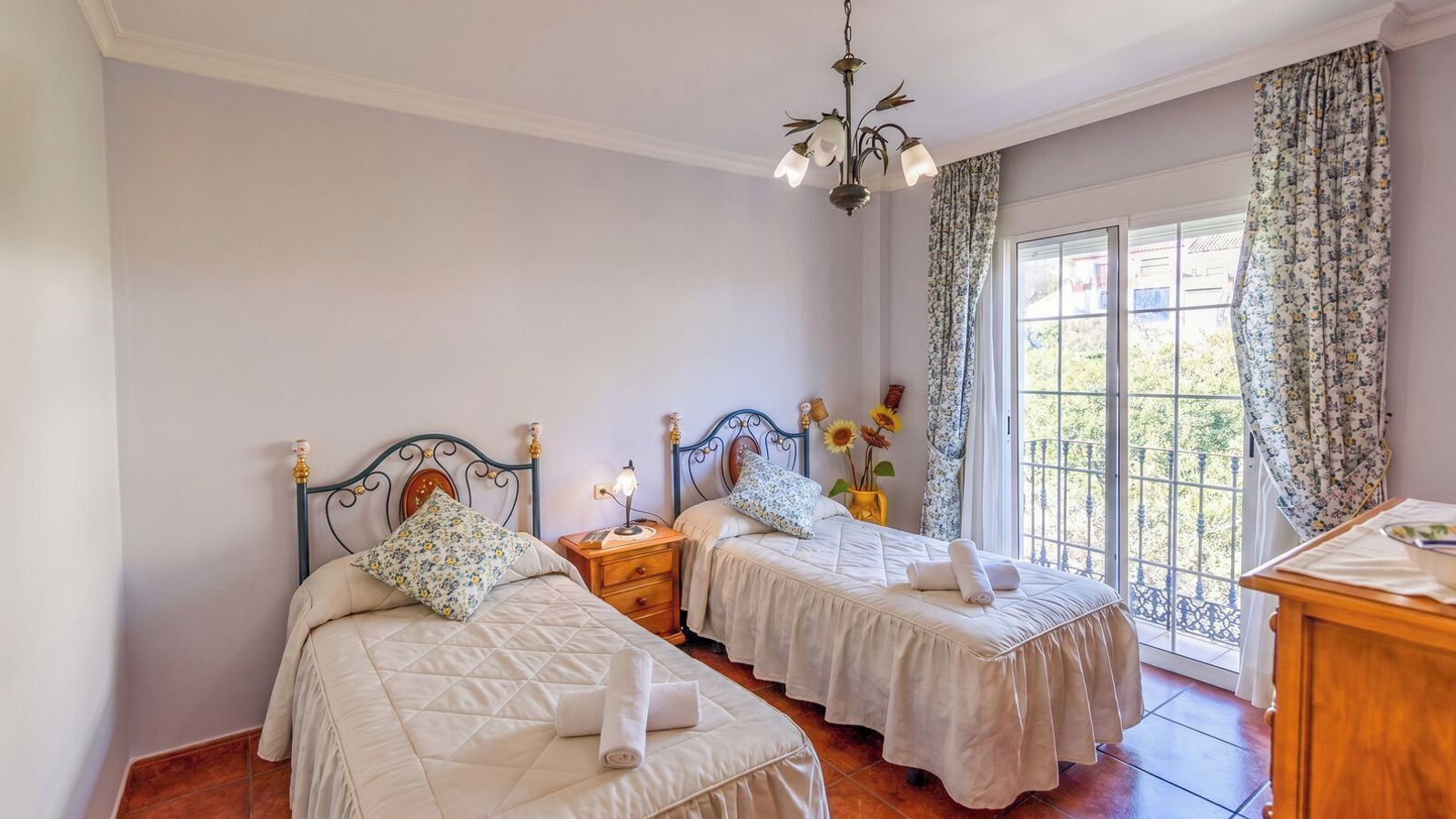 A bedroom with two beds, a chandelier, a nightstand, a window with curtains, and a wooden dresser.