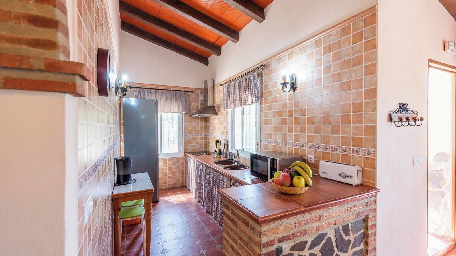 A compact kitchen with a tiled backsplash, a wooden countertop, and a fruit bowl.