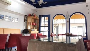 Zona pranzo con tavolo in vetro e sedie rosse, soffitto blu decorato con motivi di uccelli e vista attraverso un arco.