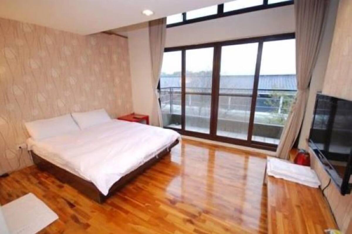 Un dormitorio con una cama grande, suelo de madera, televisor y ventana con vistas.