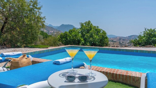 A poolside setting with two martini glasses of orange juice, a pair of sunglasses, and a white table.