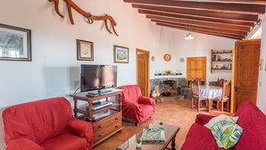Un salon avec des canapés rouges, un téléviseur posé sur un meuble en bois, une cheminée en pierre et un coin repas avec une table et des chaises.