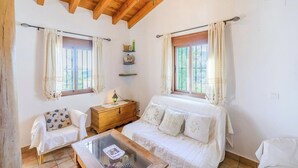 Um quarto aconchegante com cabeceira de madeira, mesa de cabeceira com abajur, sofá branco e mesa de centro de vidro.
