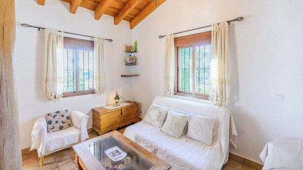 A cozy bedroom with a wooden headboard, a bedside table with a lamp, a white sofa, and a glass coffee table.
