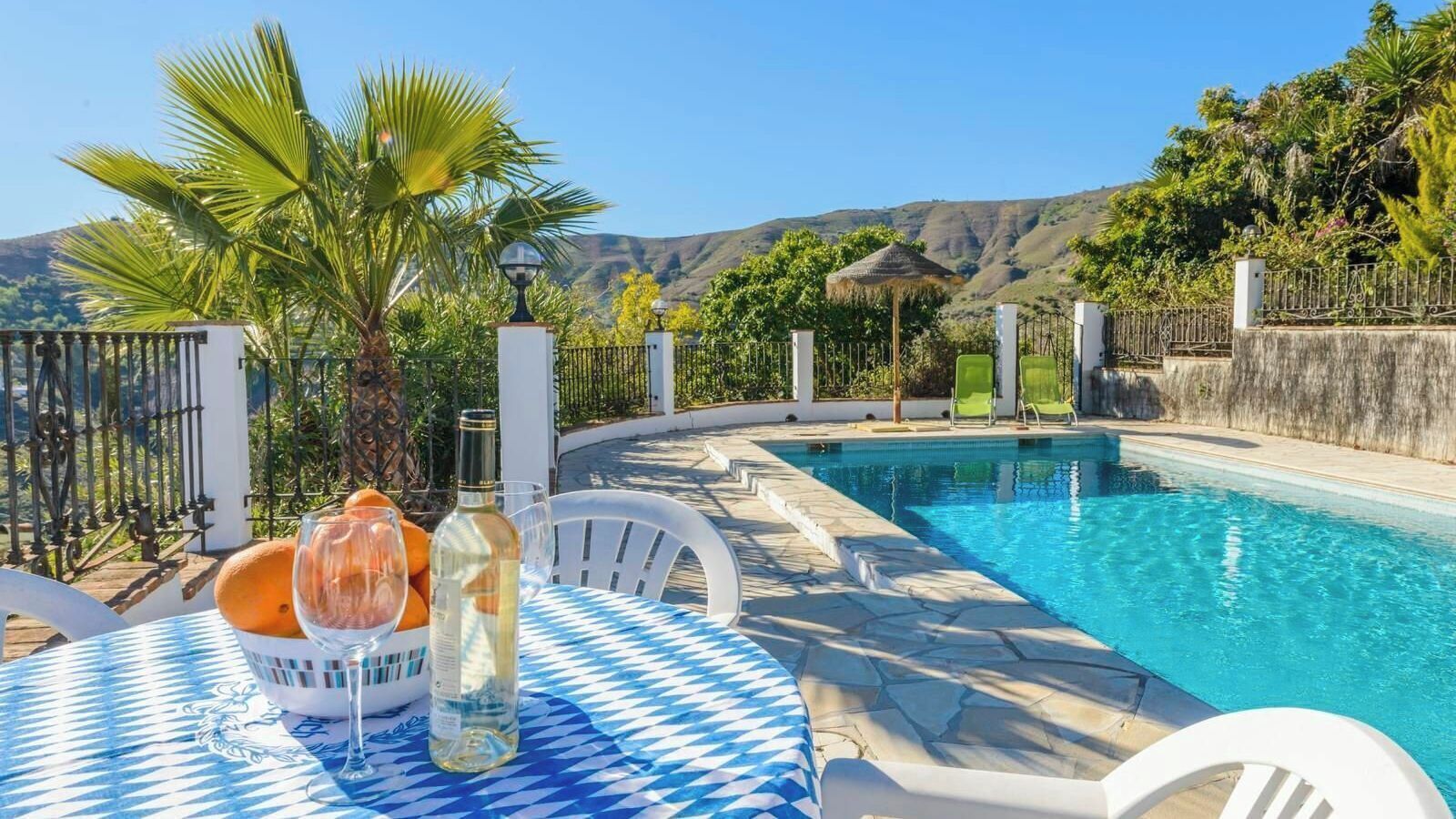 Uma área junto à piscina com mesa, cadeiras e uma garrafa de vinho.