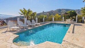 A rectangular swimming pool with a stone deck, surrounded by white lounge chairs and palm trees. - La Loma de Cútar by Ruralidays (Málaga)