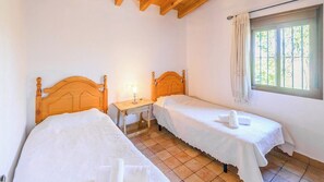 Une chambre avec deux lits simples, une petite table de chevet avec une lampe et une fenêtre avec des rideaux.