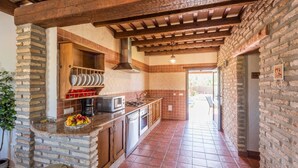 A kitchen with a stone wall, wooden beams, a tiled backsplash, and a view to the outside.