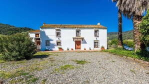 A white building with a tiled roof, a gravel driveway, and a small garden area with potted plants. - Casa del Tigre Gaucín by Ruralidays (Málaga)