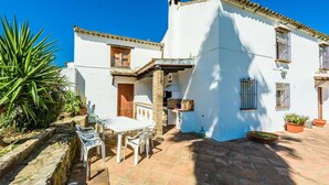 A white building with a patio area featuring a table and chairs, a stone wall, and potted plants. - Casa del Tigre Gaucín by Ruralidays (Málaga)