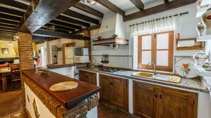 A rustic kitchen with wooden cabinets, a granite countertop, and a hanging pot rack. - Casa del Tigre Gaucín by Ruralidays (Málaga)