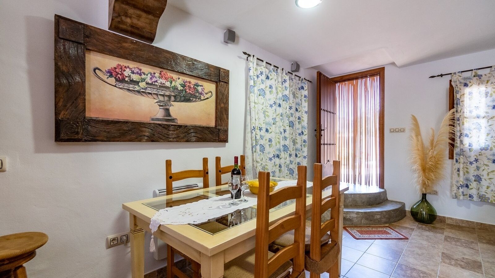 Zona pranzo con tavolo in legno, sedie, un quadro appeso e una finestra con tende.