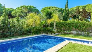 A rectangular swimming pool with clear blue water, surrounded by a well-maintained lawn and various trees and shrubs. - El Cenador Conil de la Frontera by Ruralidays (Cádiz)