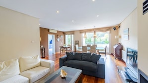 A spacious living room with a dark sofa, a light-colored sofa, and a coffee table. There is a dining area with a table and chairs, and a TV on the right side. - El Cenador Conil de la Frontera by Ruralidays (Cádiz)
