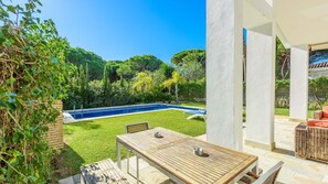 Une terrasse avec une table et des chaises en bois, une piscine et une végétation luxuriante.