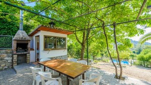A patio with a stone barbecue, a table, and chairs, surrounded by trees and a pool in the background. - El Rincón de Cazorla La Iruela by Ruralidays (Jaén)