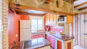 A kitchen with a stone wall, wooden beams, a refrigerator, a microwave, a sink, and a window. - El Rincón de Cazorla La Iruela by Ruralidays (Jaén)