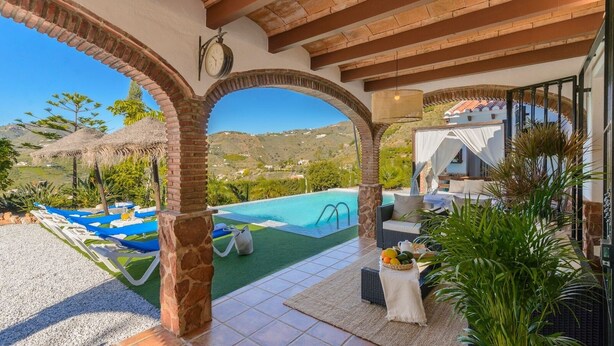 Zona piscina con vista su una montagna, un portico coperto con posti a sedere e una piscina con scaletta.