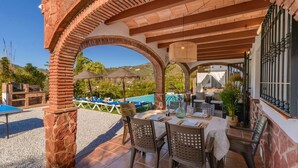 Patio esterno con tavolo apparecchiato per mangiare, circondato da sedie e area piscina sullo sfondo.