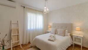 Una camera da letto con un letto grande, due comodini con lampade, una scala e una finestra con tende leggere.