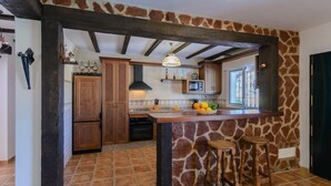 Cucina con parete a muro in pietra, mobili in legno, isola centrale con sgabelli e lampadario a sospensione.