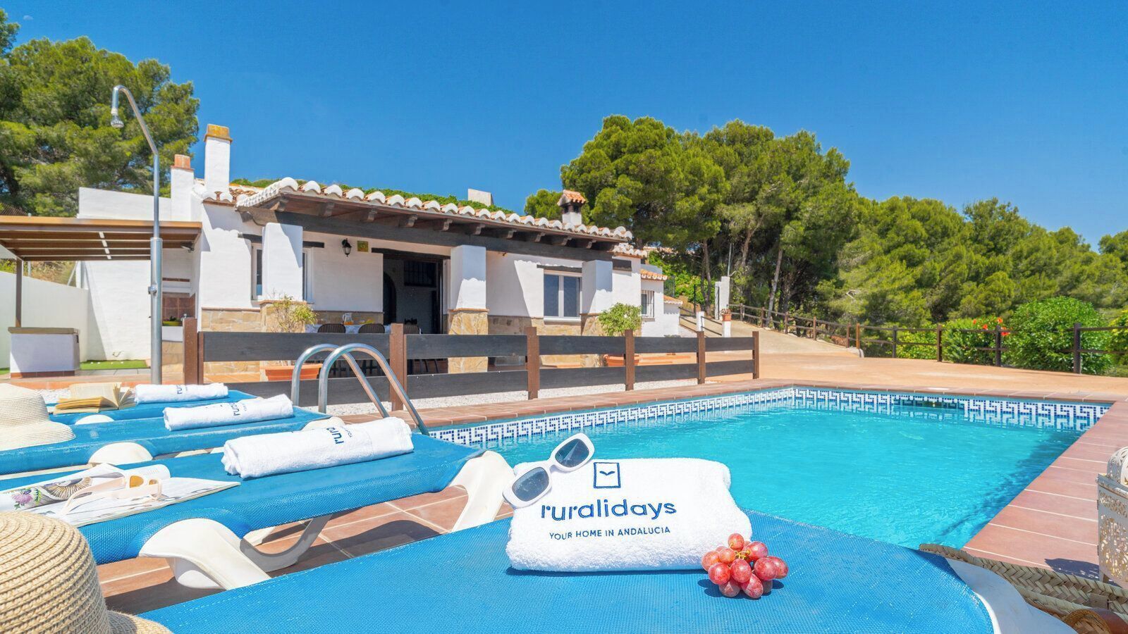 A pool area with lounge chairs, towels, and a sign reading 'Royaldays Your Home in Andalucia.'