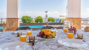 A table set for breakfast with fruit, drinks, and a view of a pool and greenery. - Lagar El Mirador Almáchar by Ruralidays (Málaga)
