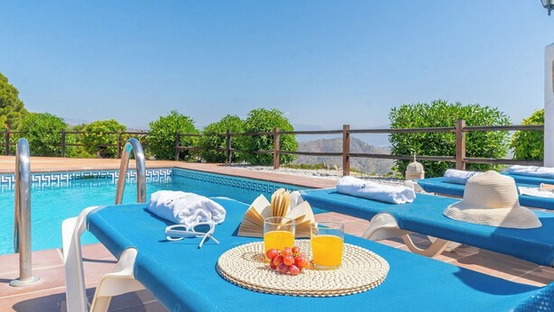 Zona junto a la piscina con sillones de descanso, piscina y vistas a las montañas.