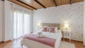 Una camera da letto con un letto, due comodini, un tavolino e una finestra con tende, più una parete decorata.
