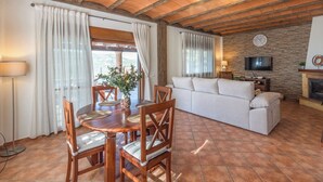 Un accogliente soggiorno con tavolo e sedie in legno, un divano bianco e una parete in pietra con un televisore.