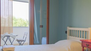 Ein Schlafzimmer mit Bett, Stuhl, Tisch und einem Fenster mit Jalousien.