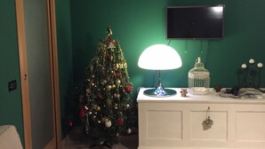 Ein Wohnzimmer mit grüner Wand, einem weißen Sofa mit Kissen im Zebra-Muster, einem Weihnachtsbaum, einer weißen Kommode und einem flachbildfernseher, der an der Wand montiert ist.