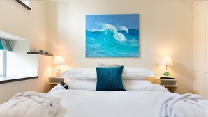 Una cama bien tendida con sábanas blancas y un cojín azul decorativo, flanqueada por dos lámparas de noche sobre mesitas auxiliares a juego.