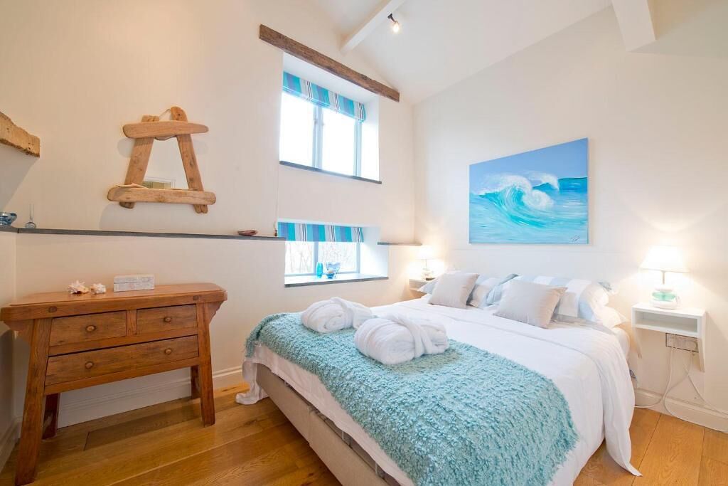 A bedroom with a bed, a wooden dresser, a painting of waves, and a window with curtains.