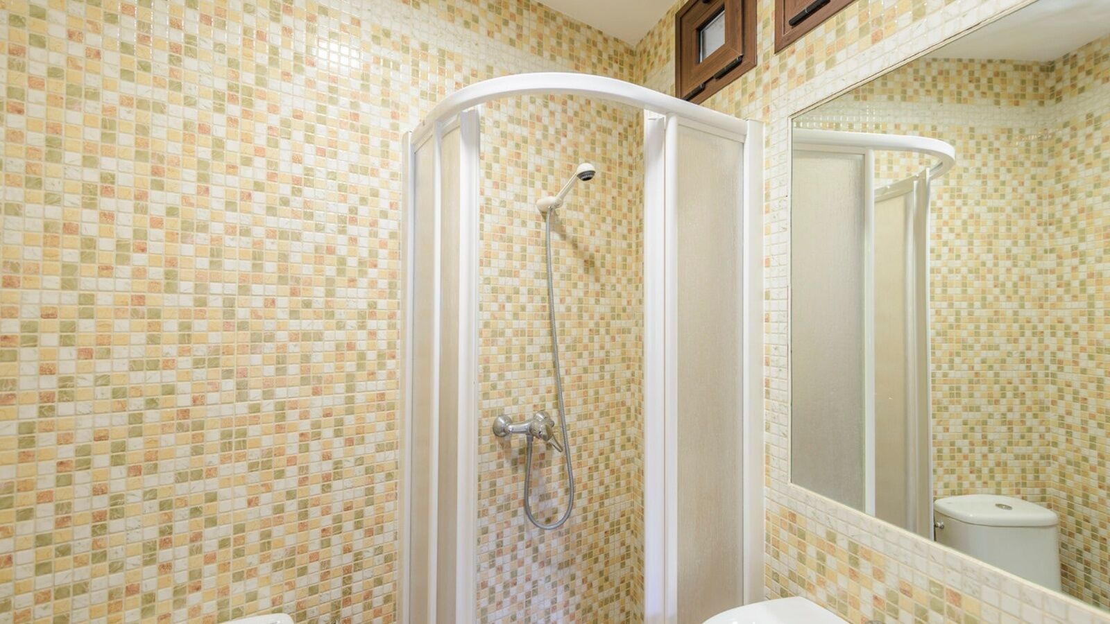 A bathroom with mosaic tile walls, a shower enclosure, a toilet, and a mirror.