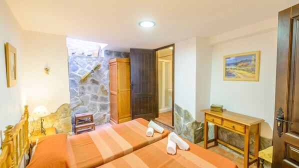 A room with two beds, a stone wall, a wooden door, a desk, and a painting on the wall. - Arados Priego de Córdoba by Ruralidays (Córdoba)