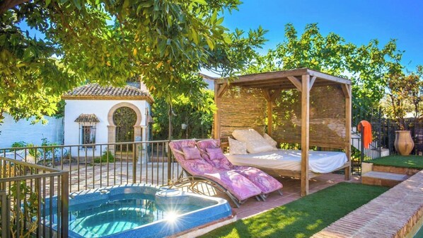 A private outdoor area with a hot tub, a covered seating area, and a small white building with an arched window.