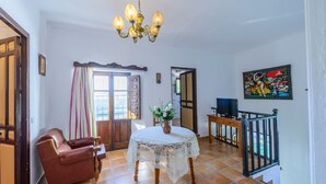 Una habitació amb una taula rodona, una cadira de cuir marró, una televisió i un quadre colorit a la paret.
