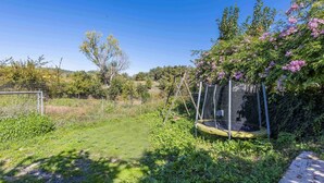 Een trampoline omgeven door groen en een houten schommelset.