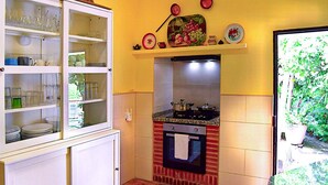 Een compacte keuken met een inbouwoven, een glazen kast met servies en een klein schapje met decoratieve objecten.