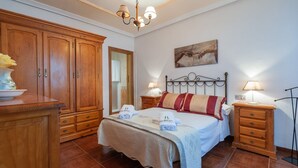 Een slaapkamer met een grote houten garderobe, een bed met hoofdeinde, twee nachtkastjes met lampen, en een schilderij aan de muur.