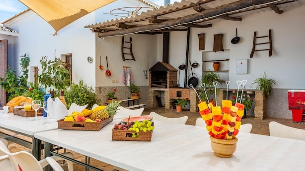 Een buitenterras met een witte tafel, gedekt met fruit en een houten schaal met fruitspiesjes.