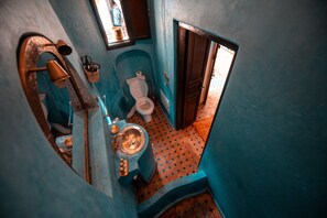 Une petite salle de bain aux murs bleus, équipée de toilettes, d’un lavabo et d’une petite fenêtre.