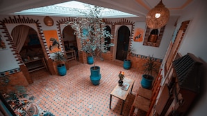 Une cour spacieuse avec un sol carrelé, des plantes en pot et une table agrémentée d’un vase.